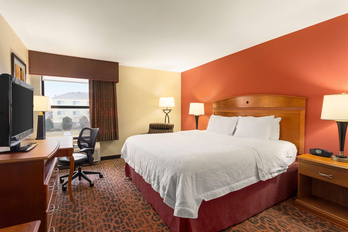 A hotel room with a bed, desk, chair, and a television.