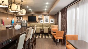 A hotel dining area with a long table, multiple chairs, a television, framed pictures on the wall, and a clock. - Hampton Inn Wichita-East (Wichita)