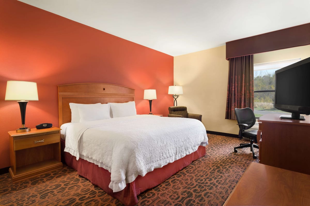 A hotel room with a large bed, two bedside lamps, a desk with a television, and a chair.