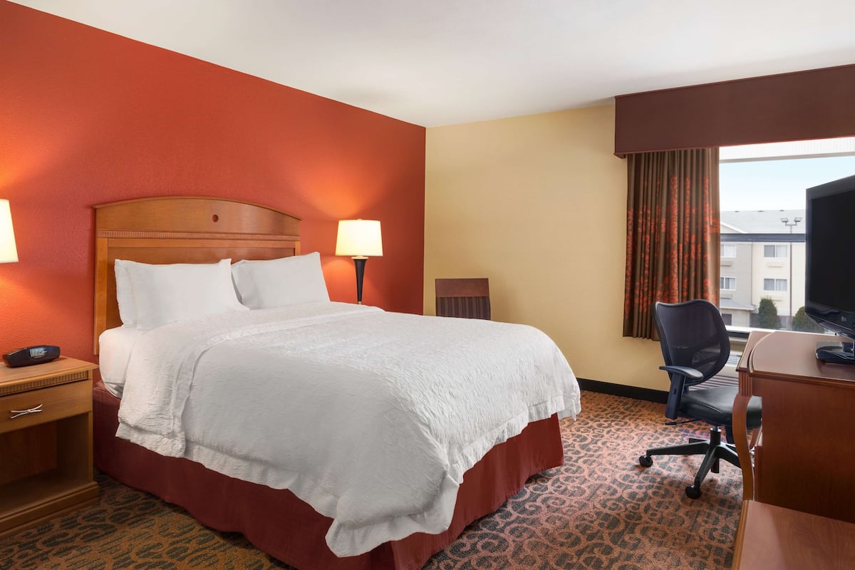 A hotel room with a large bed, a desk, a chair, a TV, and a window with curtains.