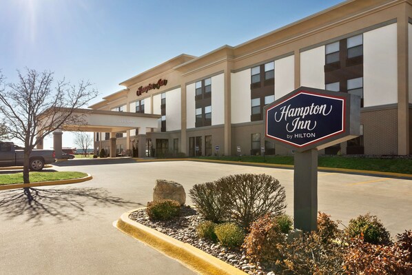 A Hampton Inn by Hilton building with a clear entrance, a parking lot, and a landscaped area with rocks and shrubs. - Hampton Inn Wichita-East (Wichita)
