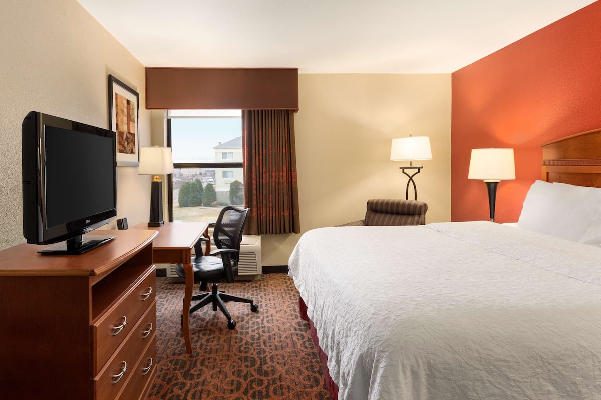 A hotel room with a bed, desk, chair, television, and two lamps.