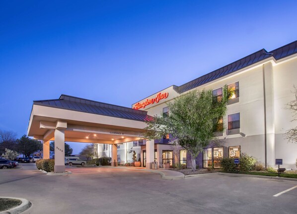 A Hampton Inn hotel with a covered entrance, a clear sky, and a parking lot.