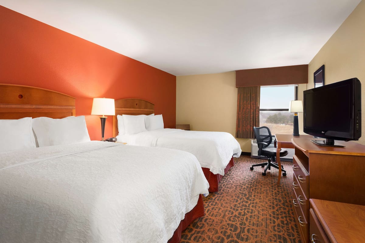 A hotel room with two beds, a desk with a television, and a view of the outdoors.