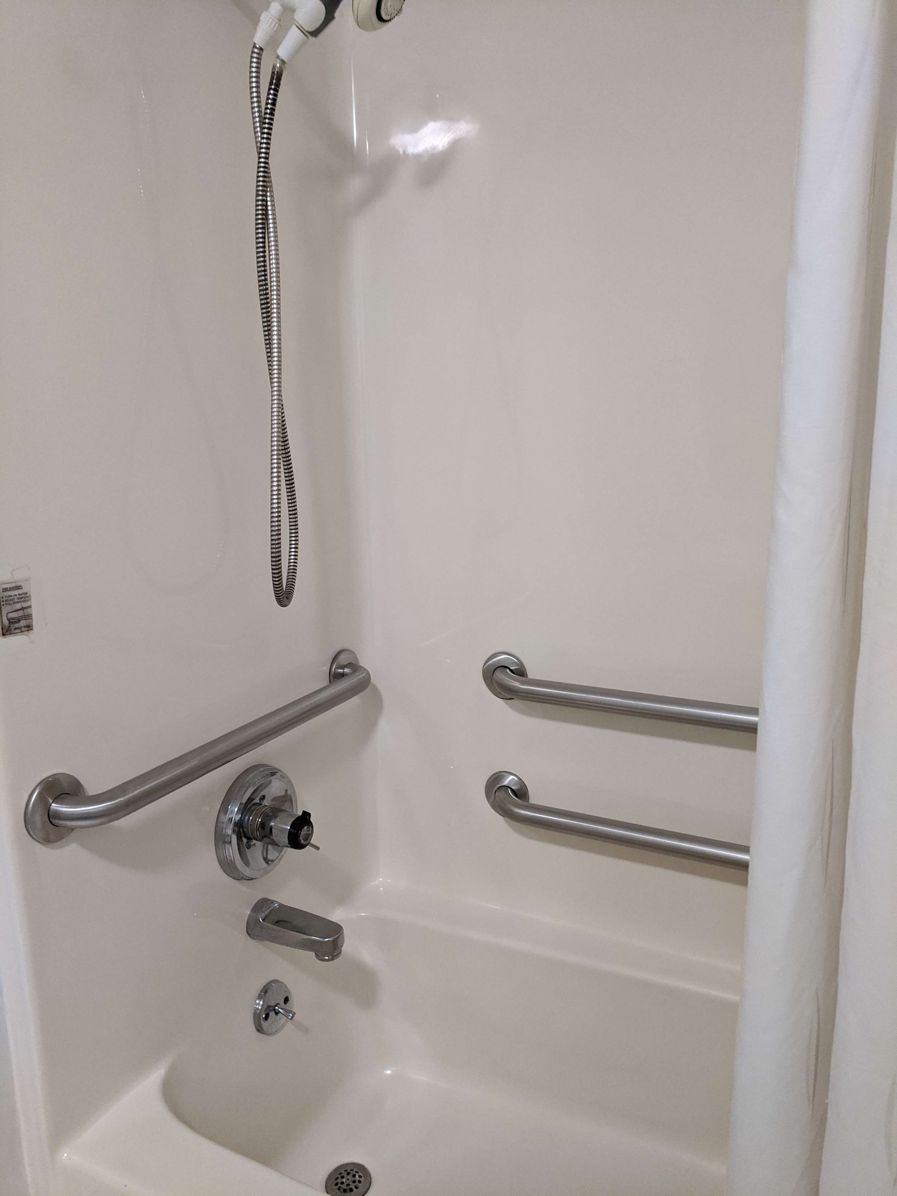 Ein Badezimmer mit einer weißen Badewanne, Haltegriffen, einer Handbrause und einem Wasserhahn.