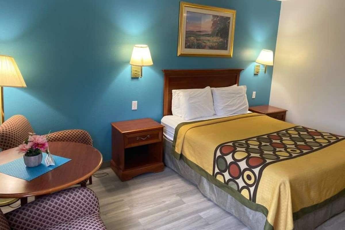 Une chambre d’hôtel avec un lit, une table de chevet, une chaise, une petite table avec une lampe et un tableau au mur.
