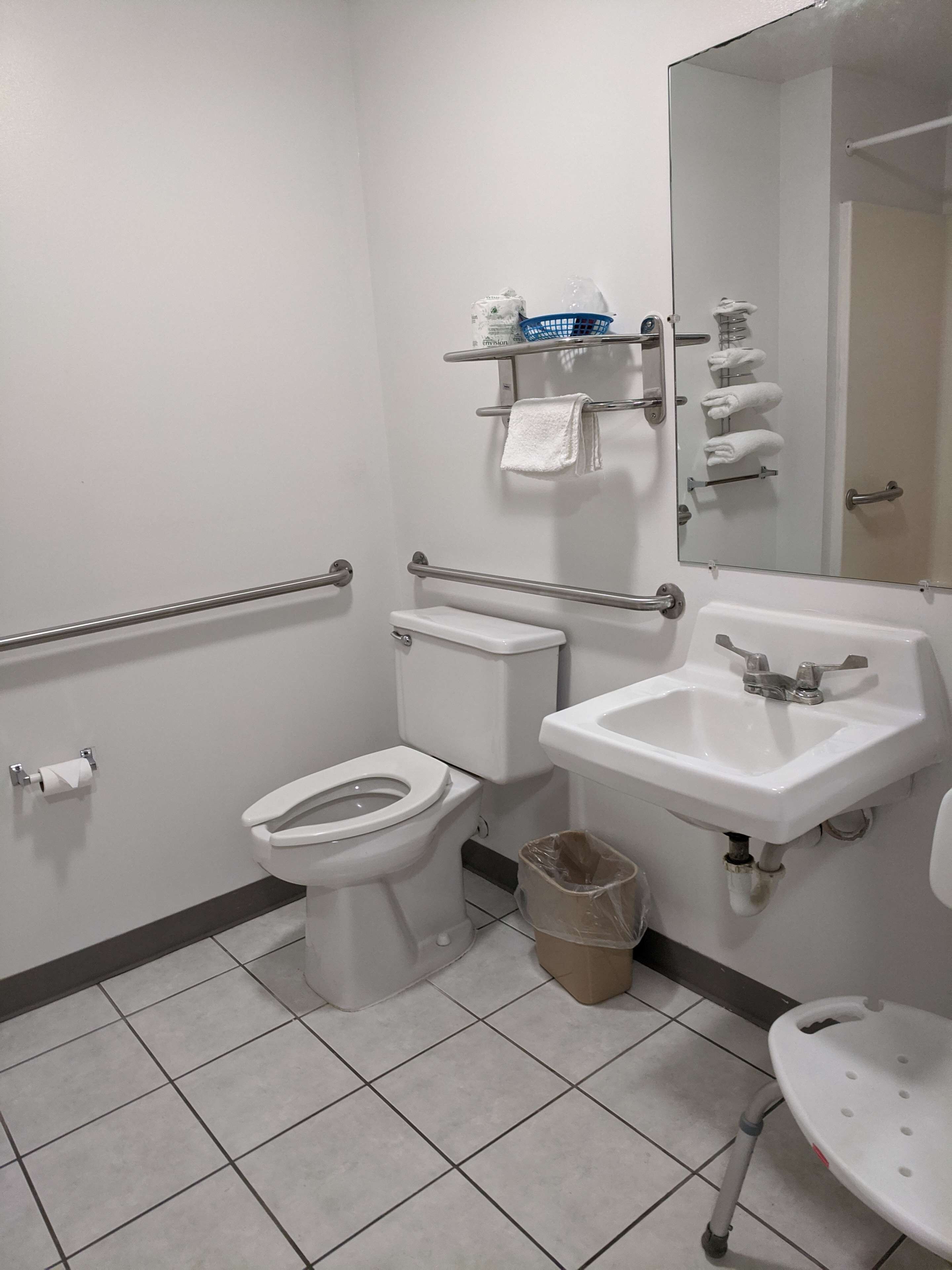 A standard hotel bathroom with a toilet, sink, and handrails.