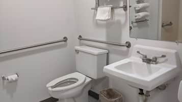 A standard hotel bathroom with a toilet, sink, and handrails.