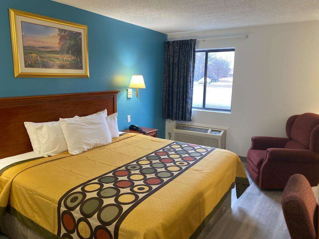 Ein Hotelzimmer mit einem großen Bett, einem Schreibtisch, einem Stuhl, einem Fenster mit Vorhängen und einem Bild an der Wand.