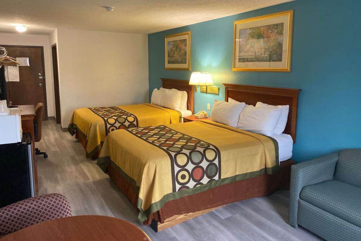 Une chambre d’hôtel avec deux lits, un bureau, une chaise et une lampe.