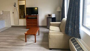 A living room with a sofa, a wooden table, a television, a microwave, and a window with curtains. - Americas Best Value Inn West Frankfort (West Frankfort)