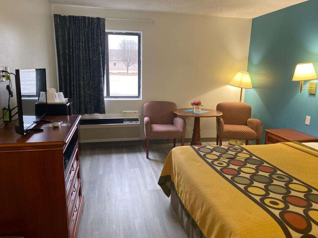 A hotel room with a bed, two chairs, a desk, a lamp, and a window with curtains.