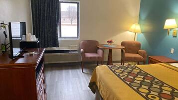 A hotel room with a bed, two chairs, a desk, a lamp, and a window with curtains.