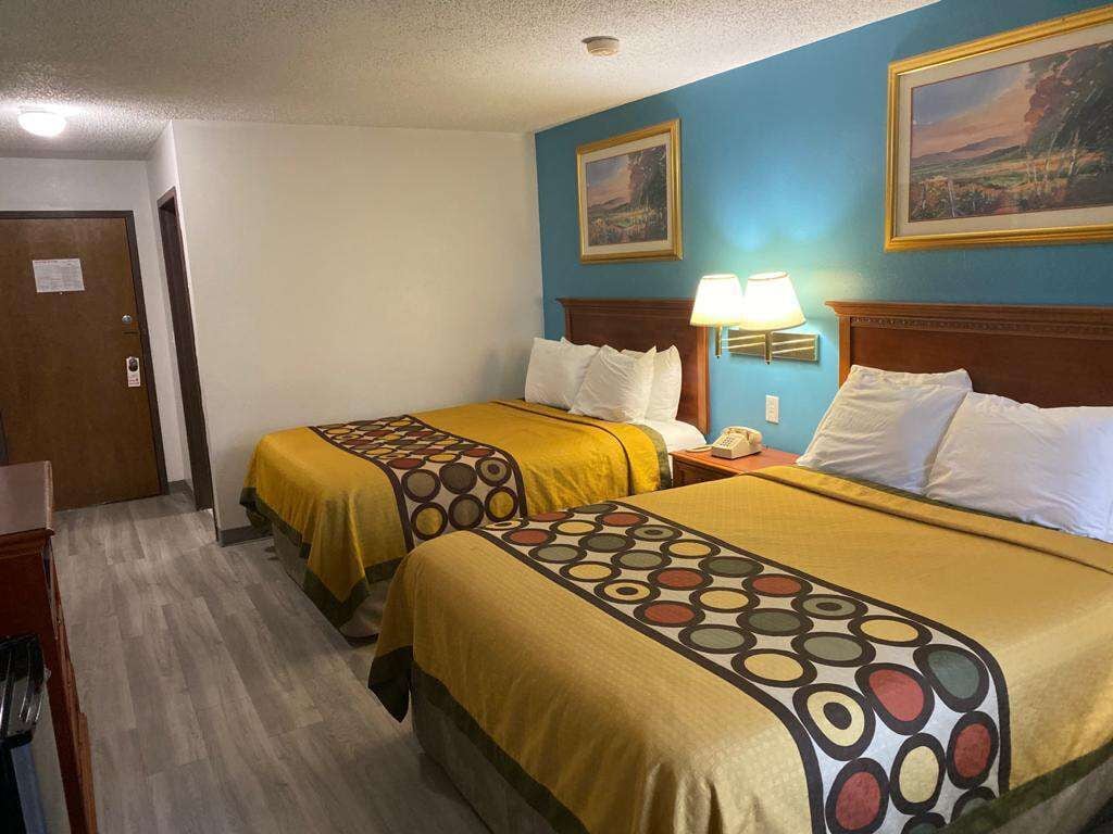A hotel room with two beds, each with a patterned bedspread, a wooden headboard, and a nightstand with a lamp.