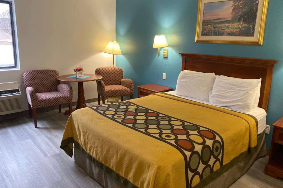 Une chambre d’hôtel avec un lit, deux chaises, une petite table et un tableau au mur.