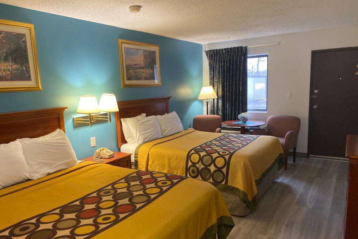 Une chambre d’hôtel avec deux lits, un bureau, une chaise et une fenêtre avec des rideaux.