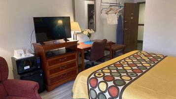 A hotel room with a bed, a desk with a computer, a TV, a microwave, and a chair.