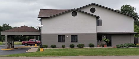 A two-story building with a flat roof, a covered parking area, and a well-maintained lawn.