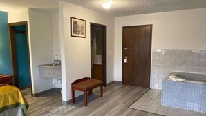 A room with a bed, a bench, a sink, a door, and a bathtub. - Americas Best Value Inn West Frankfort (West Frankfort)