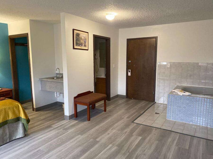 Ein Zimmer mit einem Bett, einer Sitzbank, einem Waschbecken, einer Tür und einer Badewanne.