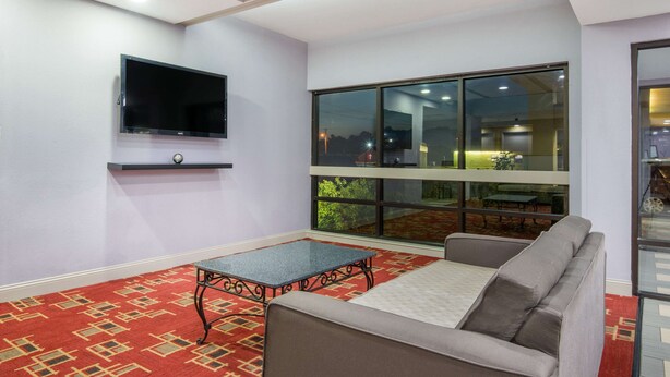 A living room with a flat-screen TV, a glass-top coffee table, a grey sofa, and a large window offering a view of the outdoors. - Super 8 by Wyndham Wichita South (Wichita)