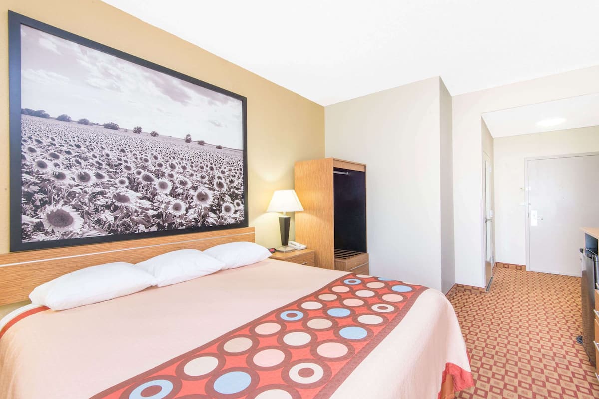 A hotel room with a large bed, a nightstand with a lamp, a wardrobe, and a door leading to another room.