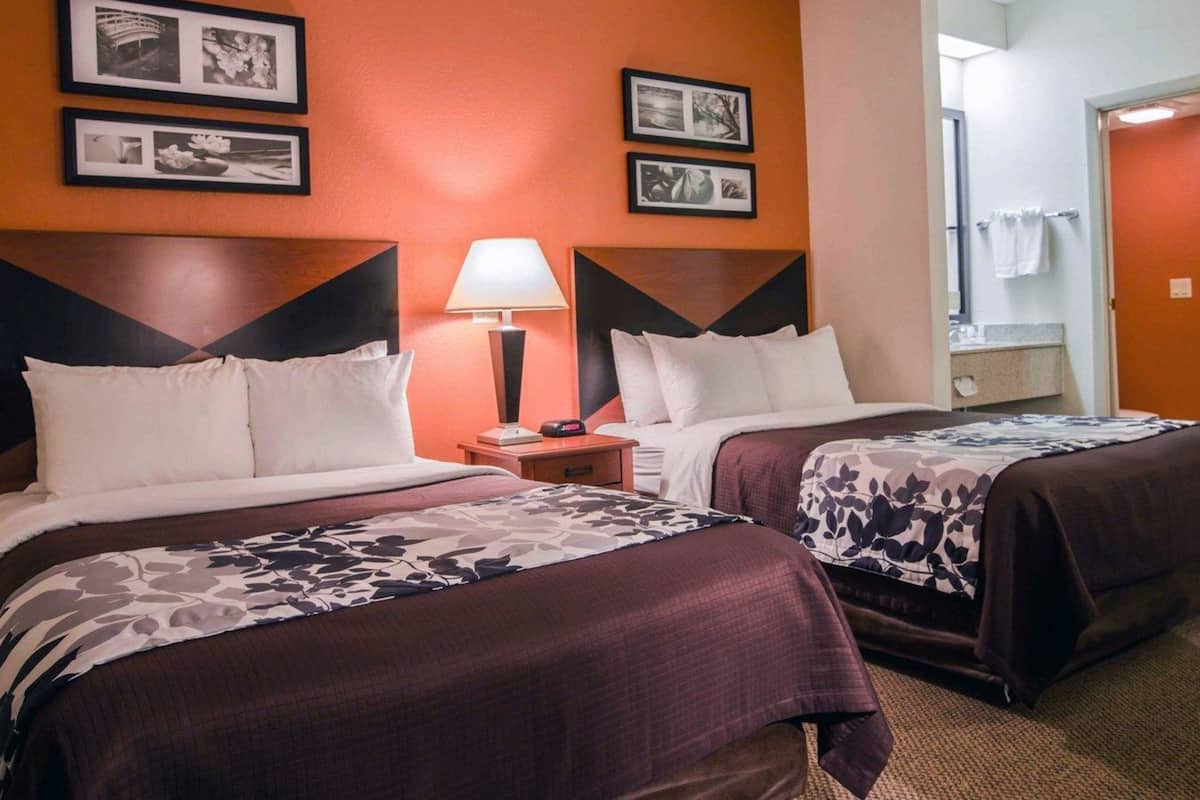 Una habitación de hotel con dos camas, una mesita de noche con lámpara y cuadros en la pared.