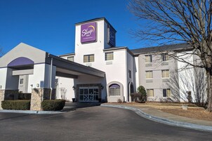 Edificio de Sleep Inn, una marca de Choice Hotels, con entrada central, varias ventanas y zona de estacionamiento.