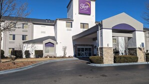 A Sleep Inn by Choice Hotels building with a modern design, featuring a prominent purple sign, a covered entrance, and a parking lot. - Sleep Inn Pelham Oak Mountain (Pelham)