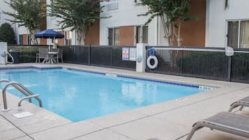 Una piscina con cerca negra, sillas de descanso y un cartel de salvavidas.