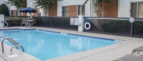 A swimming pool with a black fence, lounge chairs, and a lifeguard sign.