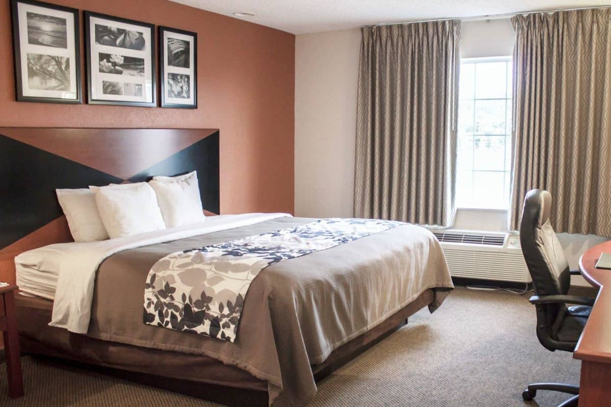 Habitación de hotel con una cama grande, un escritorio con una silla, una ventana con cortinas e imágenes enmarcadas en la pared.