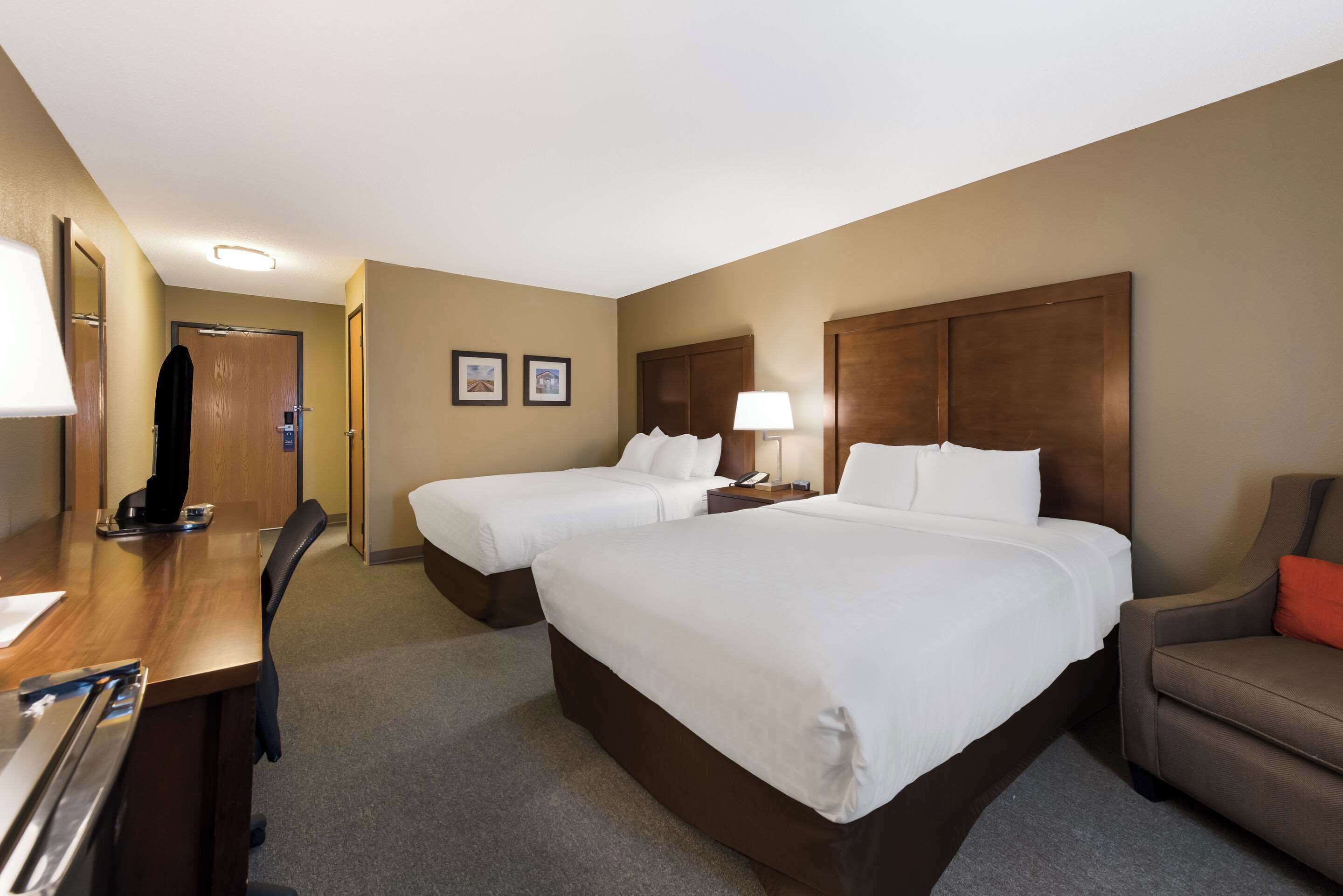 A hotel room with two single beds, a desk with a chair, a sofa, and a wooden headboard.