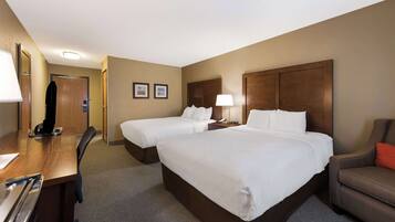 A hotel room with two single beds, a desk with a chair, a sofa, and a wooden headboard.