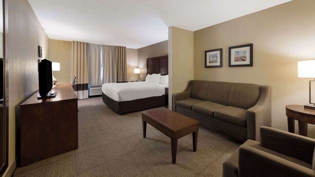 A hotel room with a bed, a sofa, a coffee table, and a TV on a stand. - Comfort Inn Wichita East (Wichita)