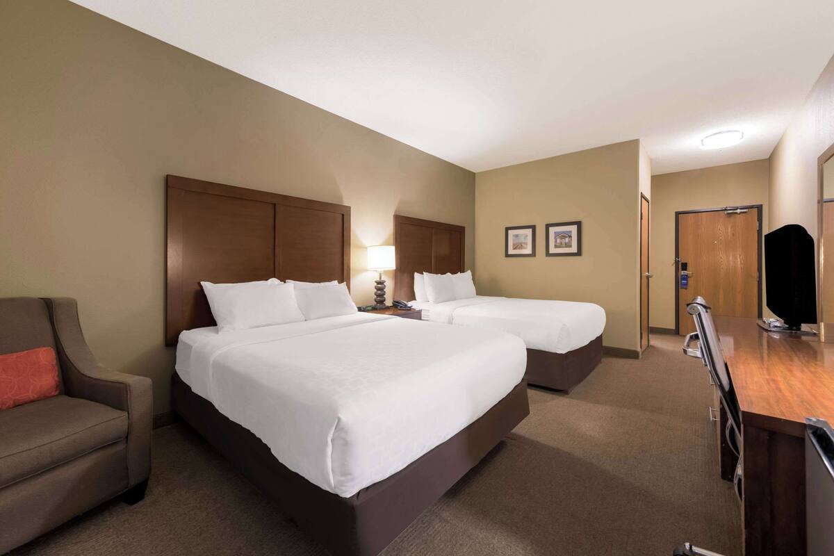 A hotel room with two beds, a desk, a chair, and a television.