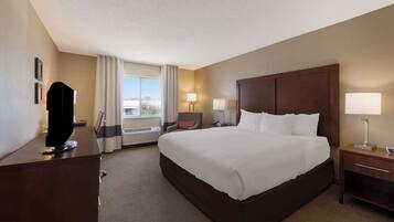 A hotel room with a large bed, a desk, a chair, a TV, and a window with curtains.