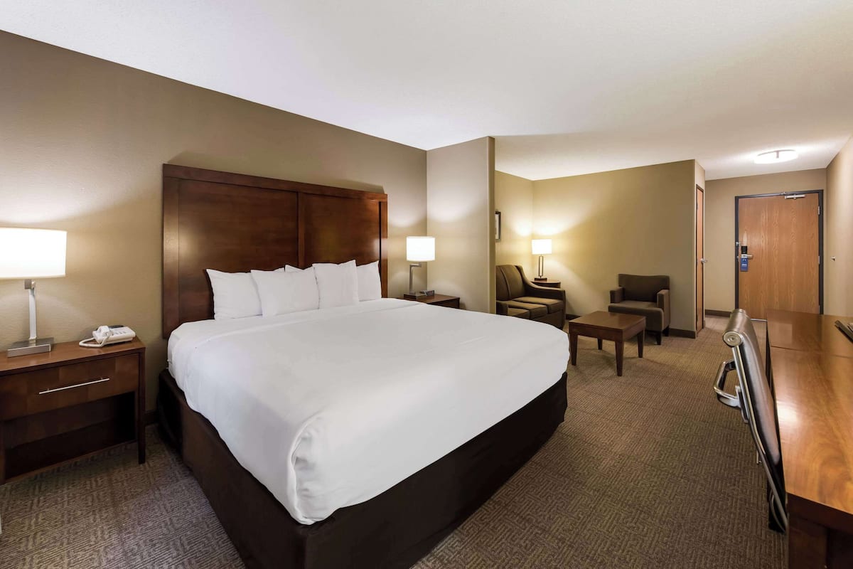 A hotel room with a large bed, bedside tables, a desk, a chair, and a door.