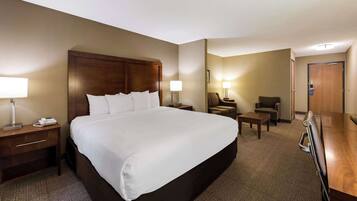 A hotel room with a large bed, bedside tables, a desk, a chair, and a door.