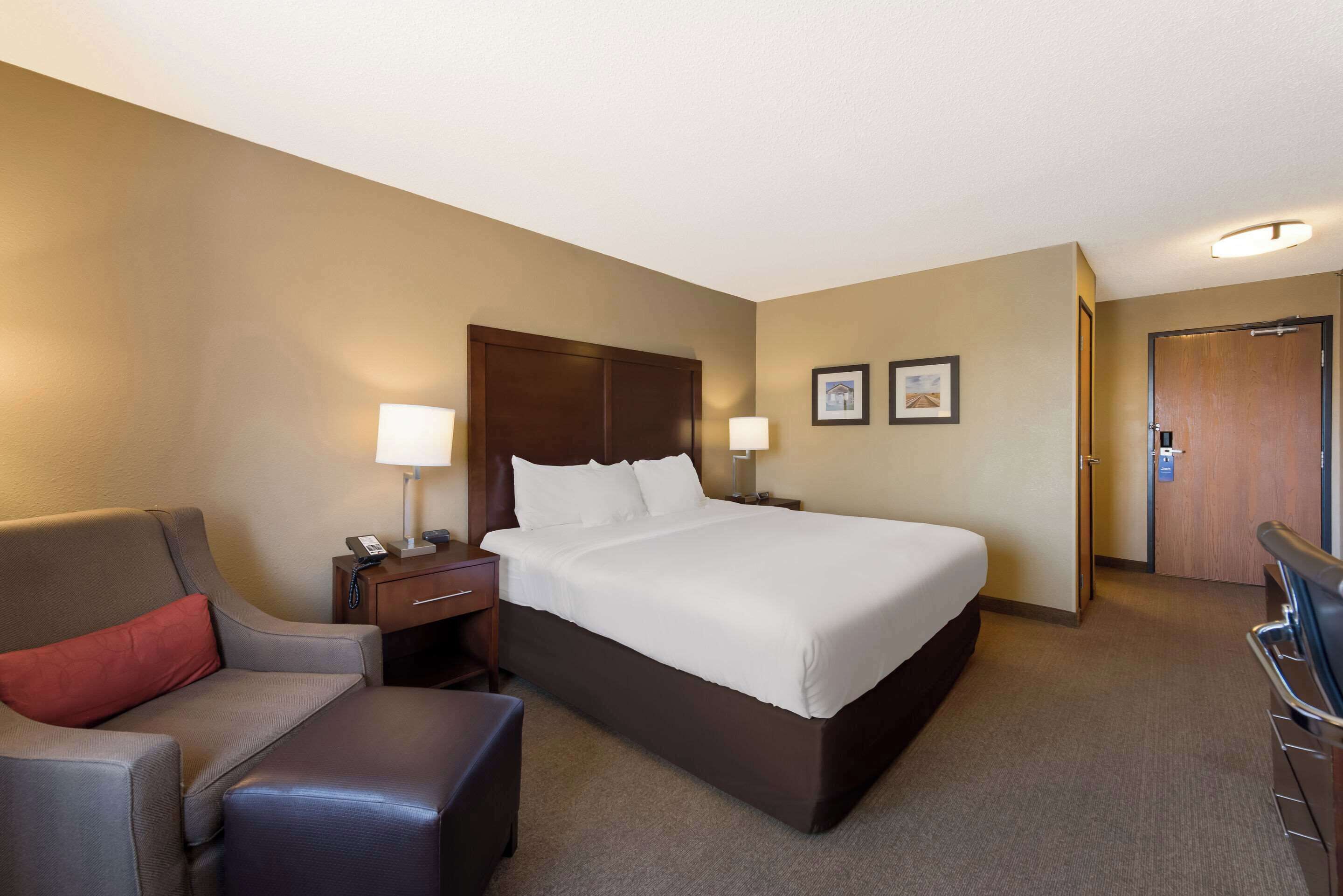 A hotel room with a large bed, a desk with a lamp, a chair, and a sofa.