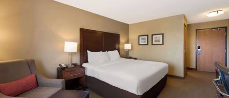 A hotel room with a large bed, a desk with a lamp, a chair, and a sofa.