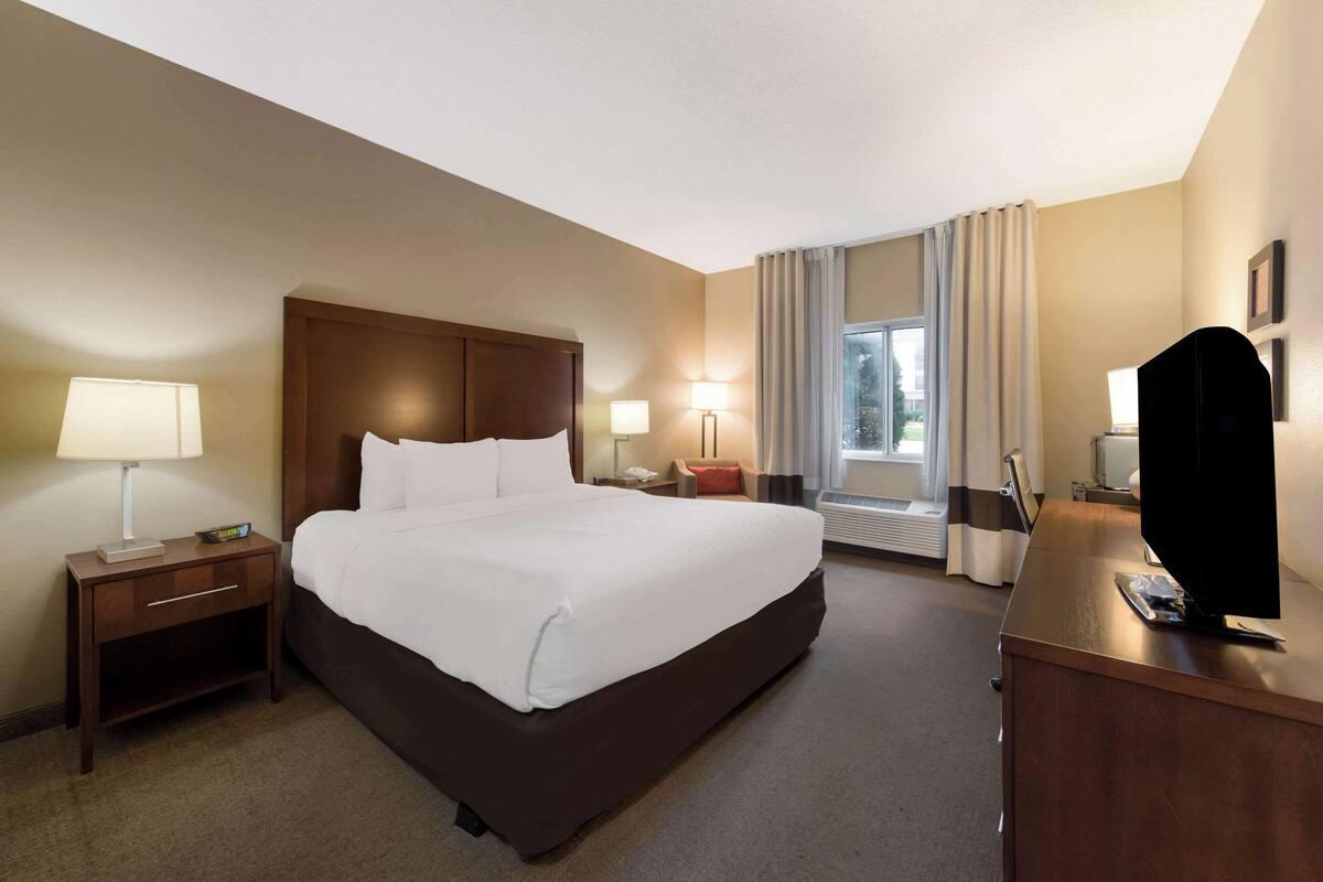 A hotel room with a large bed, bedside tables, a desk, and a window with curtains.