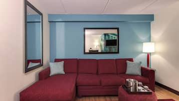 A red sectional sofa with patterned cushions, a side table with a lamp, and a tray with kitchenware.