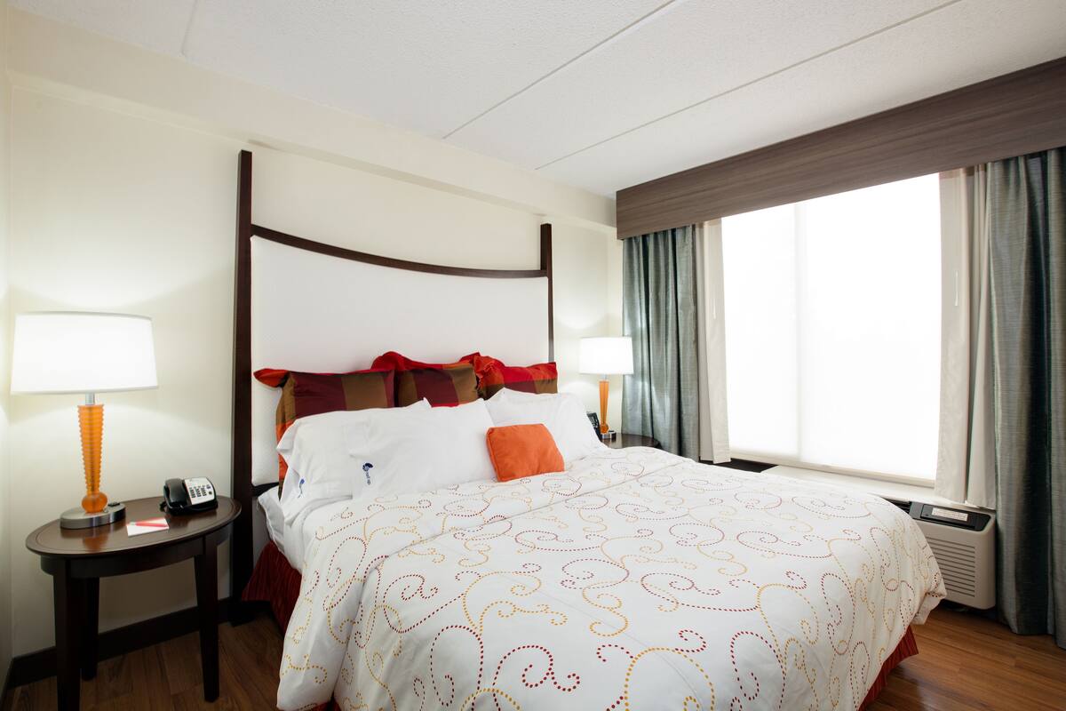 A hotel room with a four-poster bed, two bedside tables, a lamp, a phone, and a window with curtains.