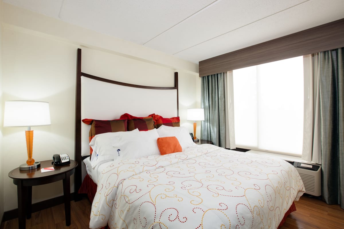 Une chambre d’hôtel avec un lit à baldaquin, deux tables de chevet, une lampe, un téléphone et une fenêtre avec des rideaux.