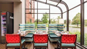 Un restaurante con cerramiento de vidrio, cabinas tapizadas en rojo y verde, un refrigerador de Coca-Cola y vistas al exterior.