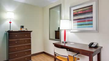 Una habitación de hotel con un aparador de madera, un escritorio con una silla, un teléfono, una lámpara y un cuadro abstracto enmarcado en la pared.