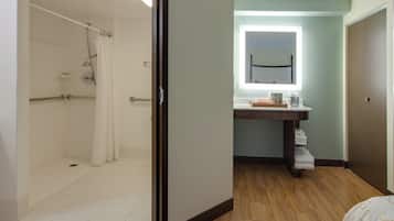 Un baño de hotel con ducha, lavamanos y espejo.
