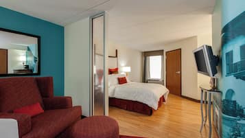 Una habitación de hotel con una cama, un sillón rojo, un televisor y un cuadro en la pared.