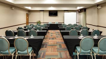 Un salón de conferencias con mesas y sillas dispuestas en filas, suelo alfombrado y una pizarra.